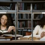 Two women studying in a library, immersed in books and learning.