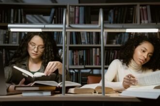 Two women studying in a library, immersed in books and learning.